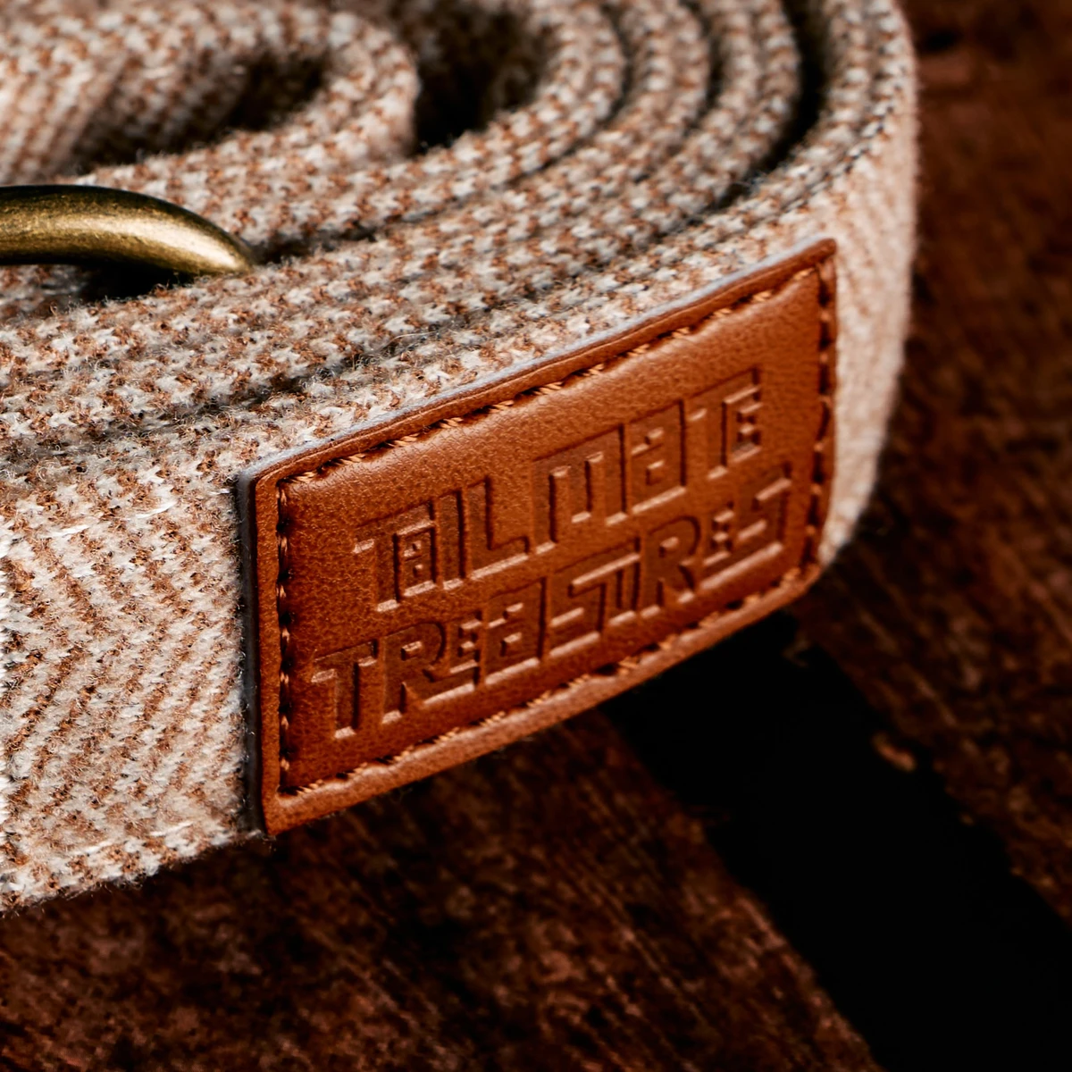 Close-up of brown herringbone fabric, stitching and the Tailmate Treasures badge on wood